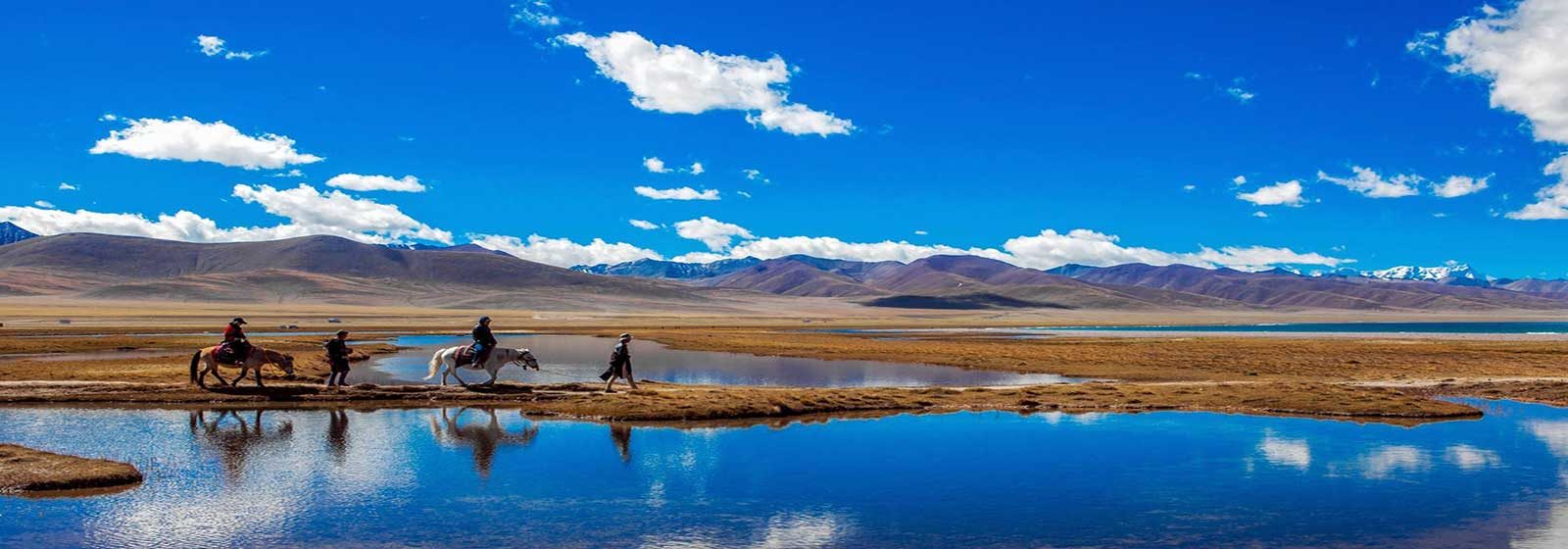 Riders by the water near Namtso Lake under white summer clouds