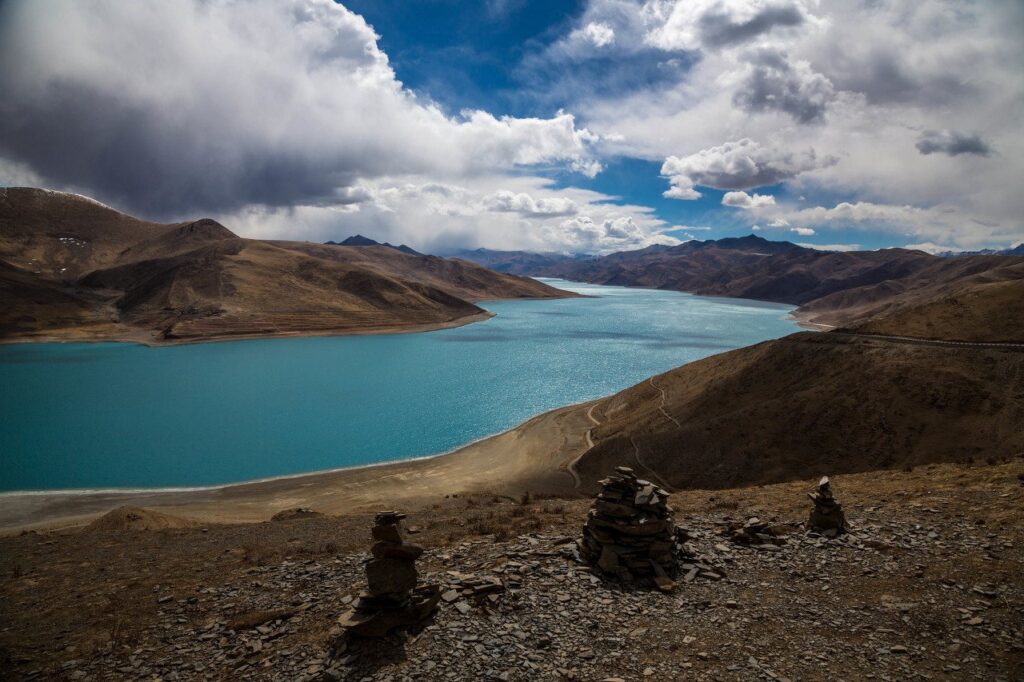 Turquoise Yamdrok Lake under spring clouds in late March, with stone cairns on the pass