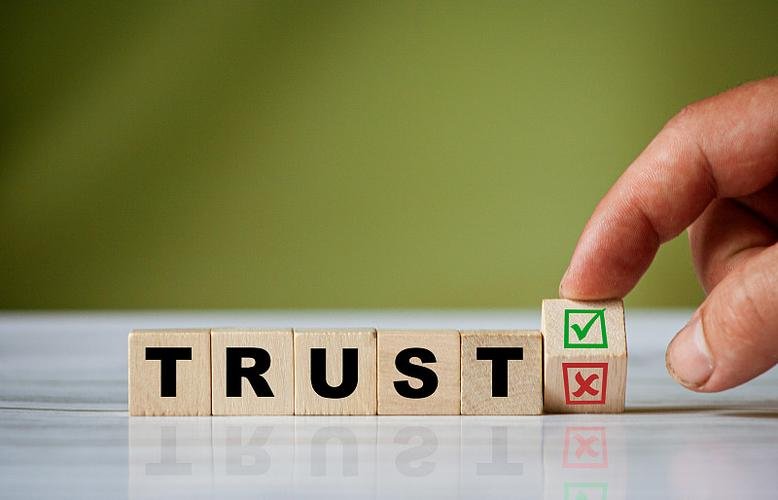 Wooden blocks spelling TRUST with a hand placing a check mark