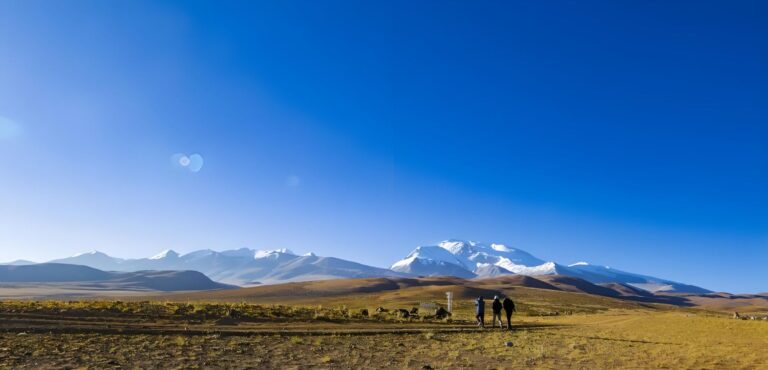 Travellers walking on the open plateau below snow peaks
